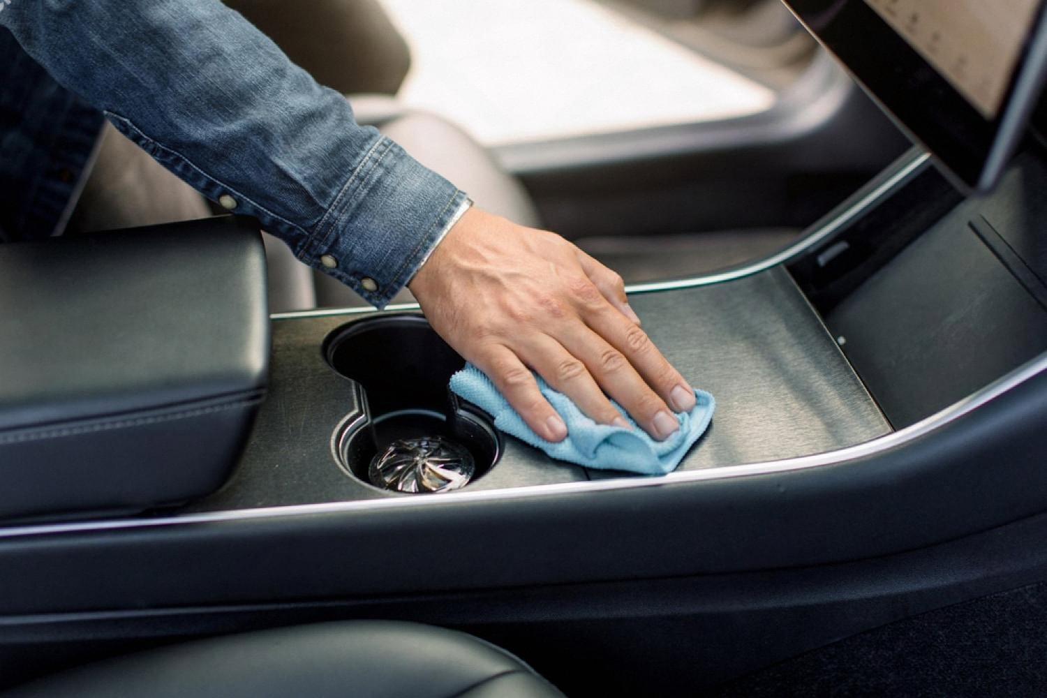 Hand wiping a car center console with a microfibre cloth during interior cleaning